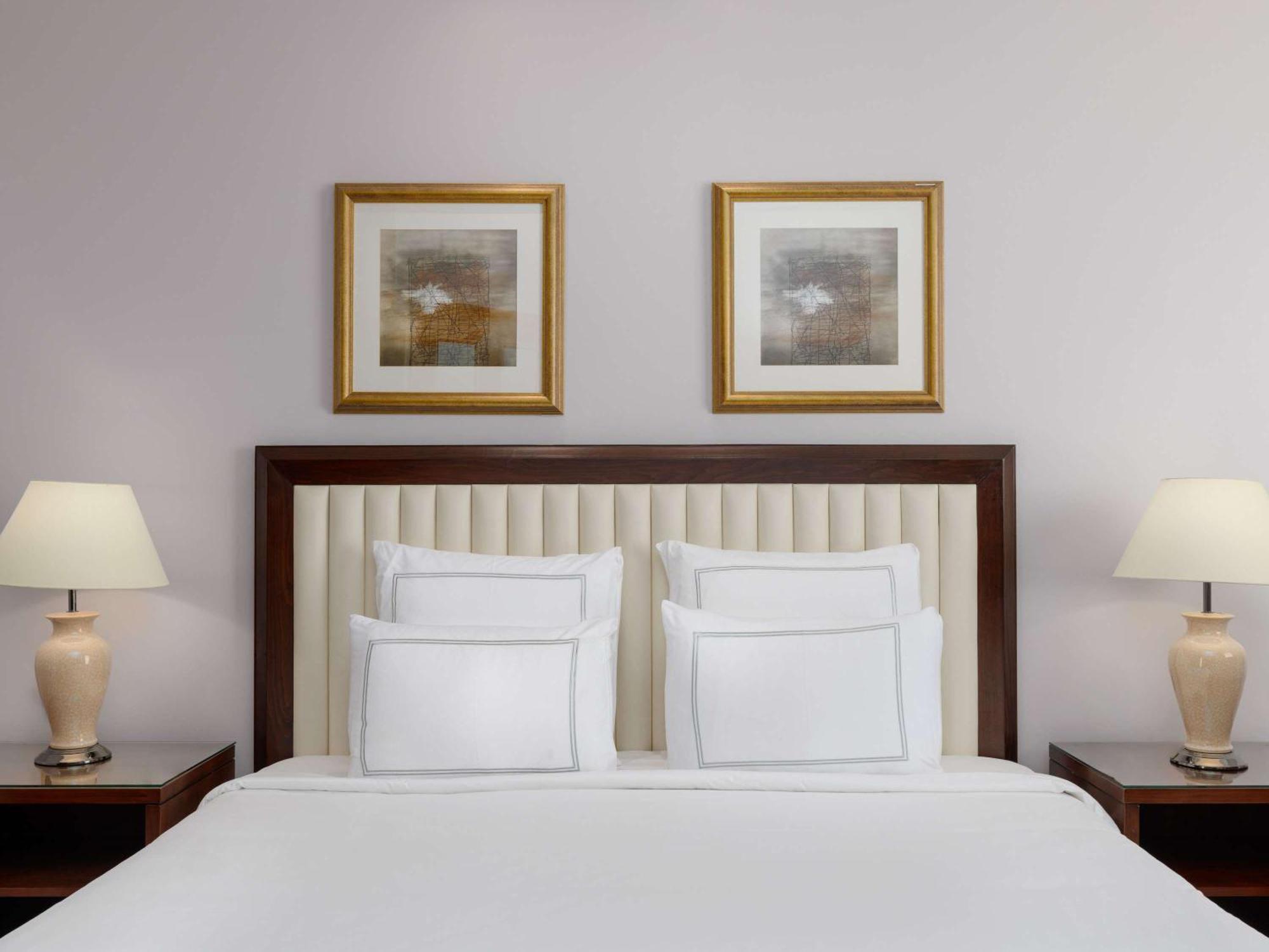 Swissotel Al Maqam Makkah Mekka Buitenkant foto The photo shows a well-decorated bedroom. The focal point is a neatly made bed with white bedding and several white pillows. Behind the bed, there is an upholstered headboard that has a vertical panel design. On either side of the bed, there are beds