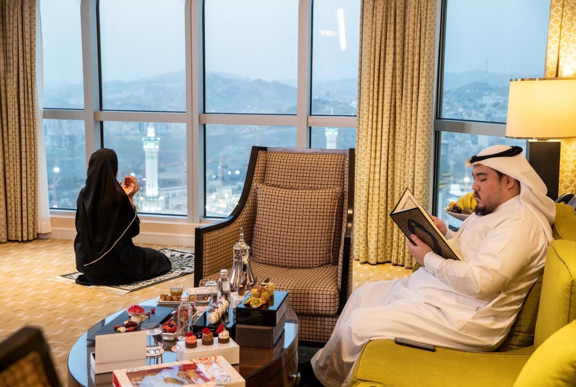 Swissotel Al Maqam Makkah Mekka Buitenkant foto The photo depicts a scene inside a hotel room or a suite with large windows providing a view of a cityscape, likely near a landmark. 

In the foreground, there is a stylish coffee table adorned with several decorative items, possibly including small 