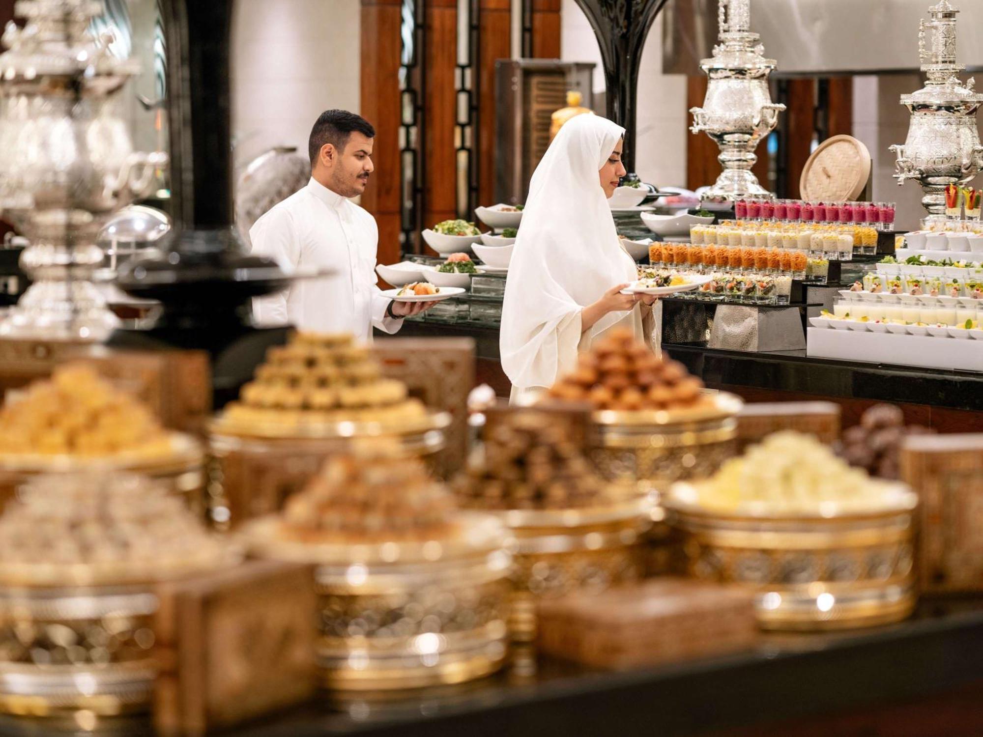 Swissotel Al Maqam Makkah Mekka Buitenkant foto The photo depicts a beautifully arranged display of traditional desserts and sweets. In the foreground, there are multiple decorative containers filled with various sweets, showcasing an assortment of vibrant colors and textures. In the background, t