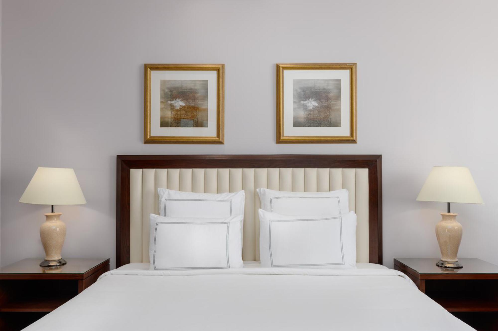 Swissotel Al Maqam Makkah Mekka Buitenkant foto The photo showcases a neatly arranged bedroom. It features a bed with a light-colored, tufted headboard and several white pillows neatly placed on it. On either side of the bed, there are wooden nightstands with lamps that have a soft, warm light. Ab